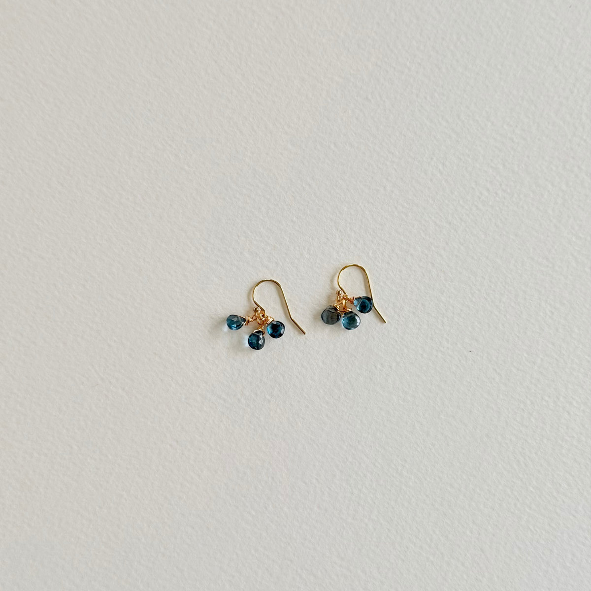 Pair of gold earrings with blue stones on a light gray background