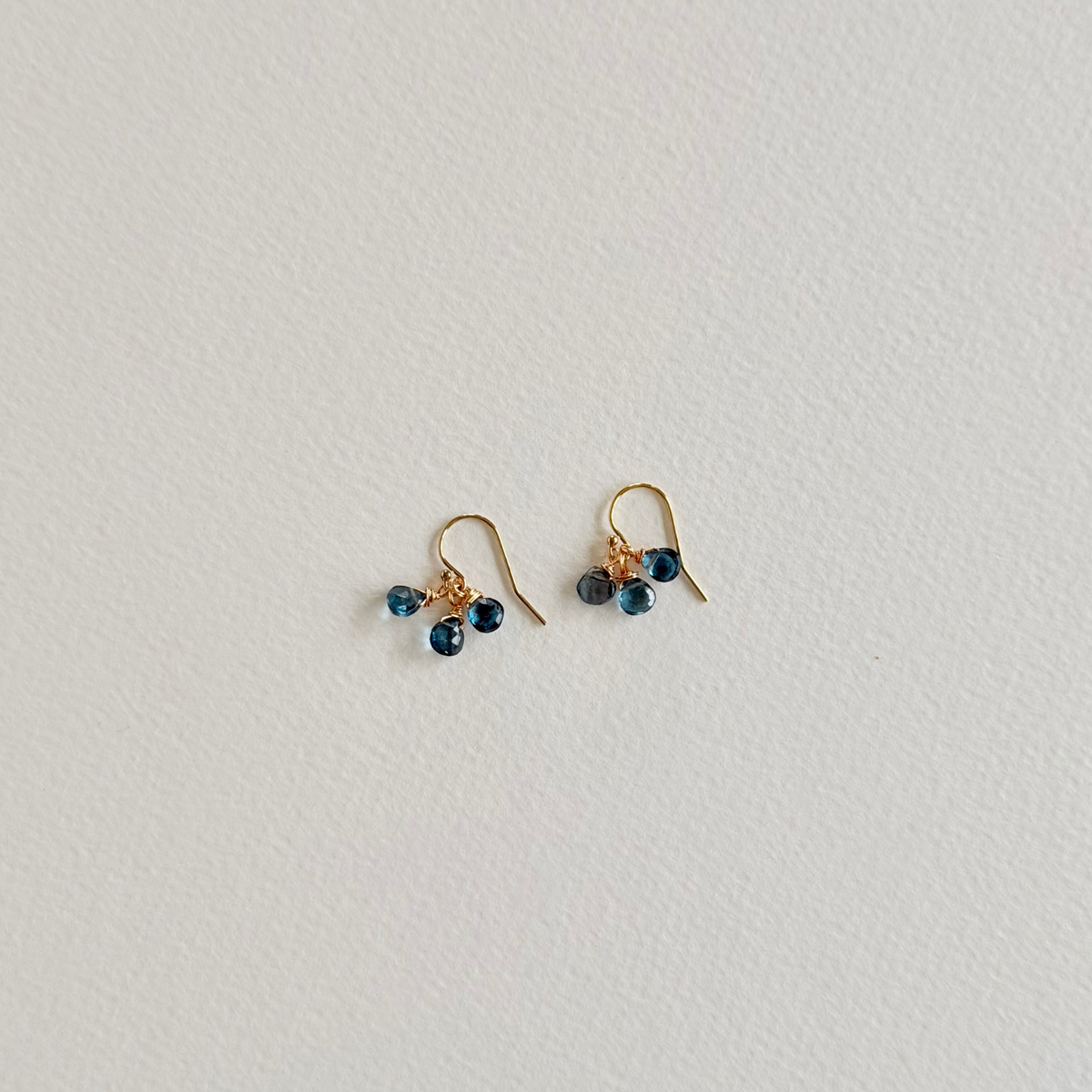 Gold earrings with blue beads on a light gray background