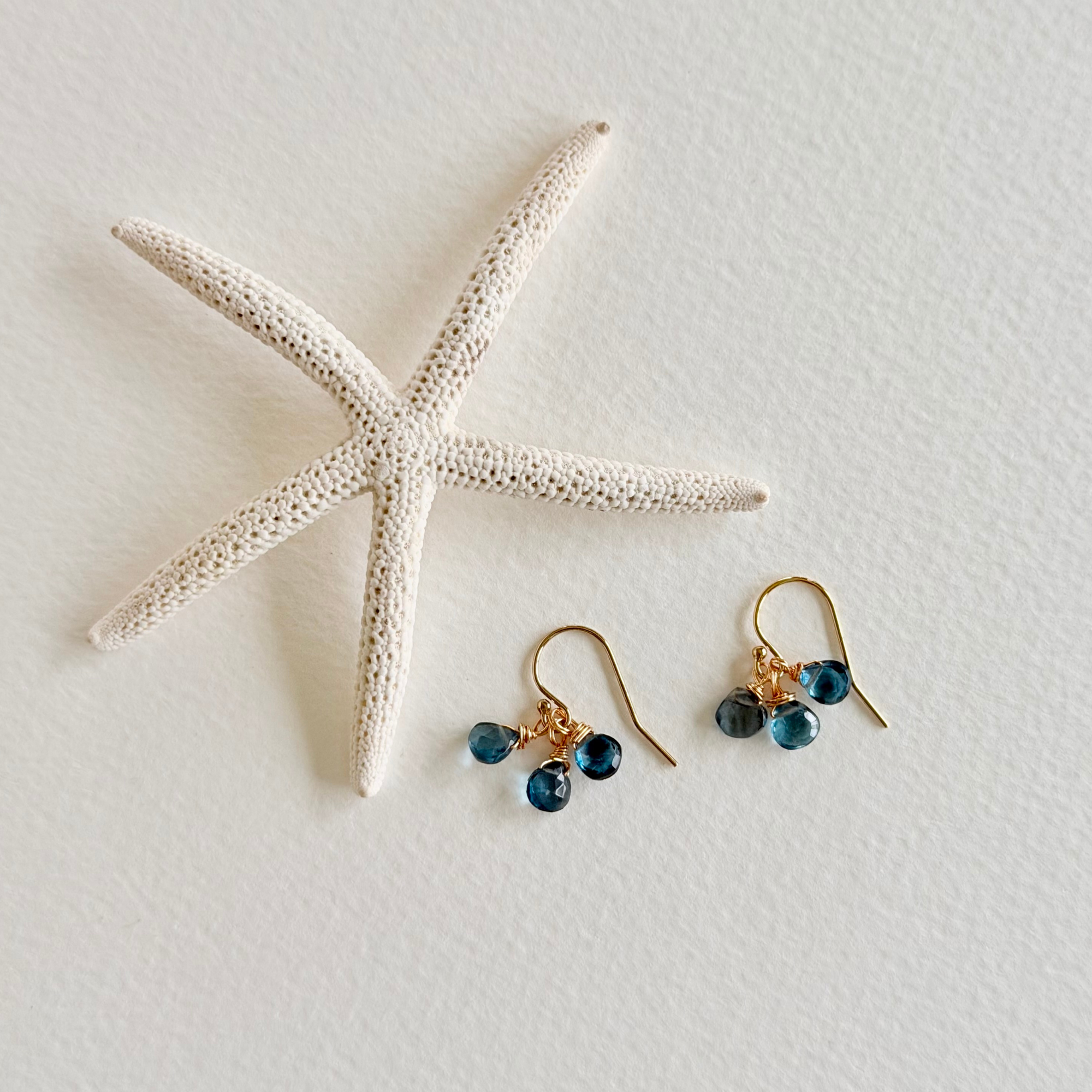 Pair of gold earrings with blue beads on a white surface with a starfish.