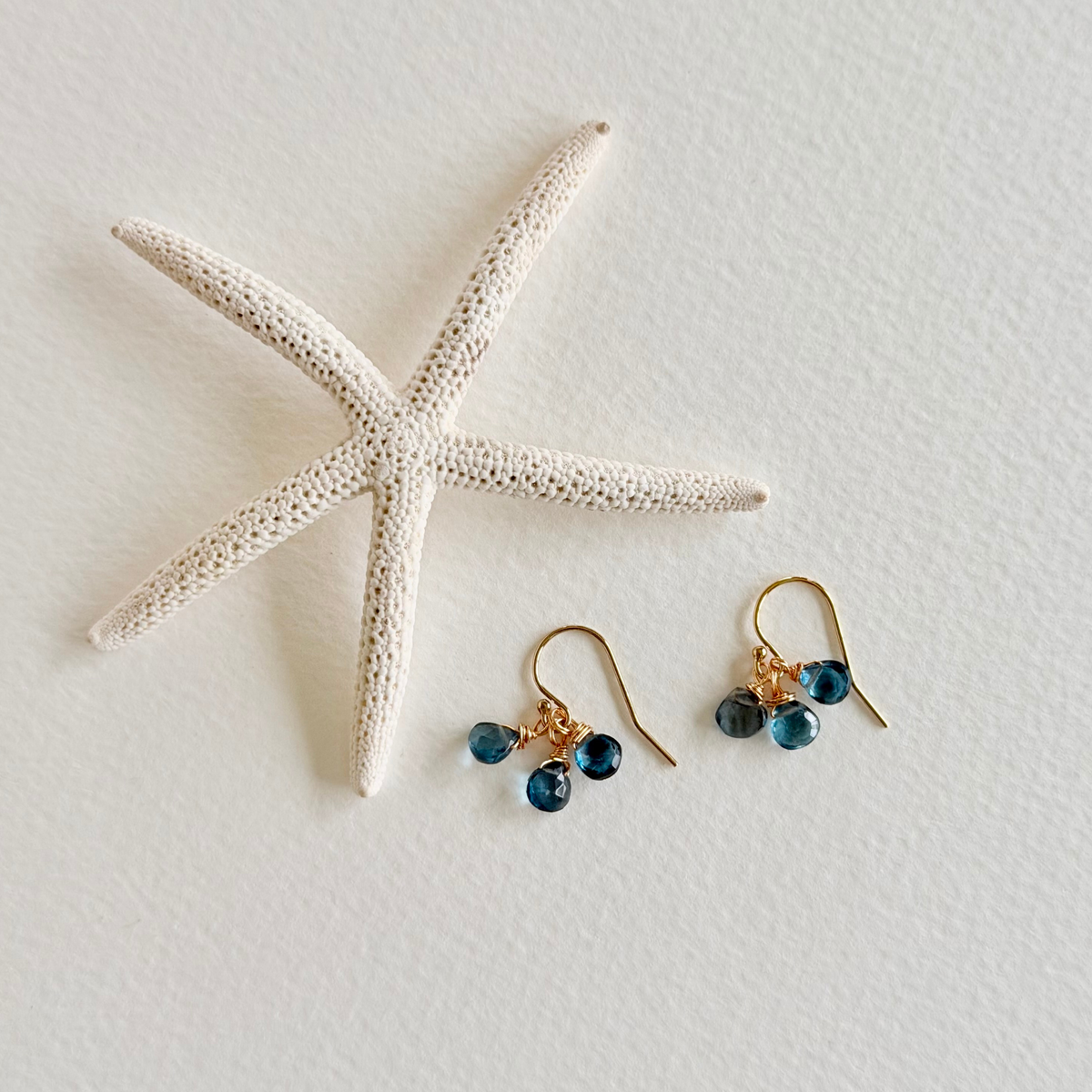 Pair of gold earrings with blue beads on a white surface with a starfish.