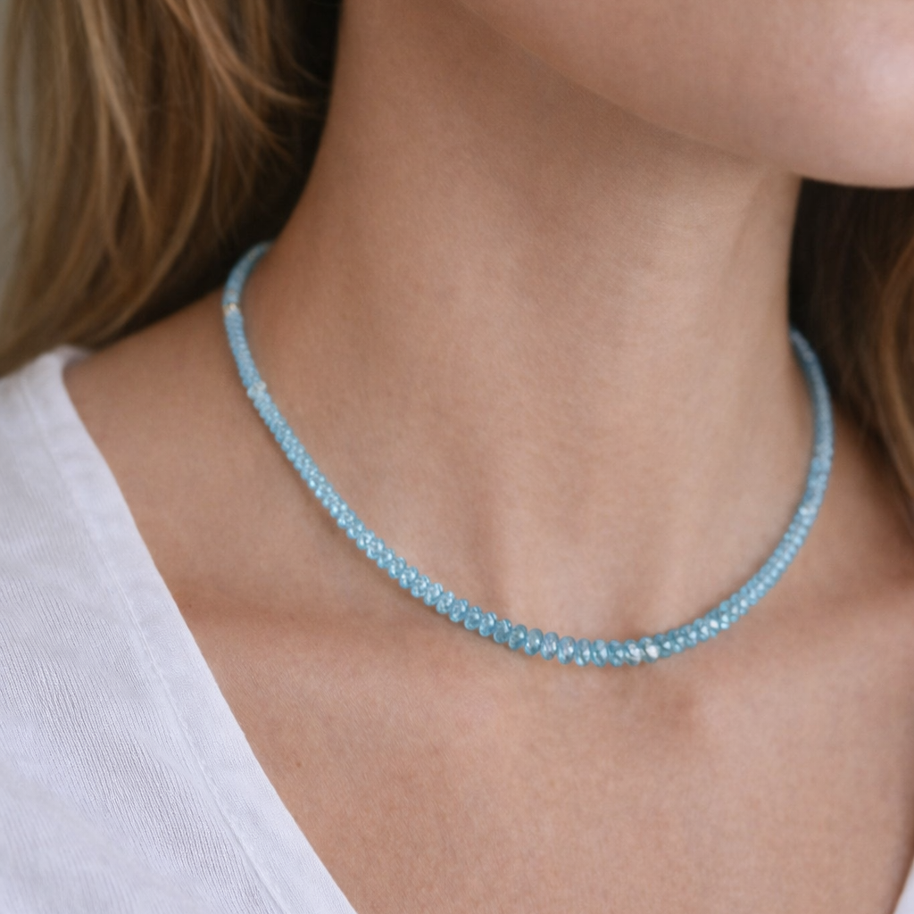 Close-up of a person wearing a light blue beaded necklace against a neutral background
