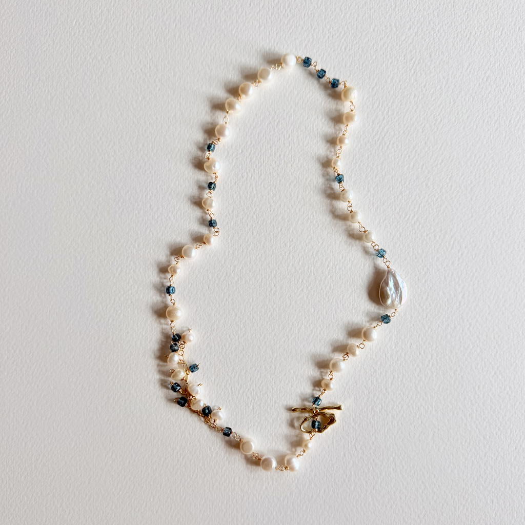 Pearl necklace with small blue beads on a light gray background