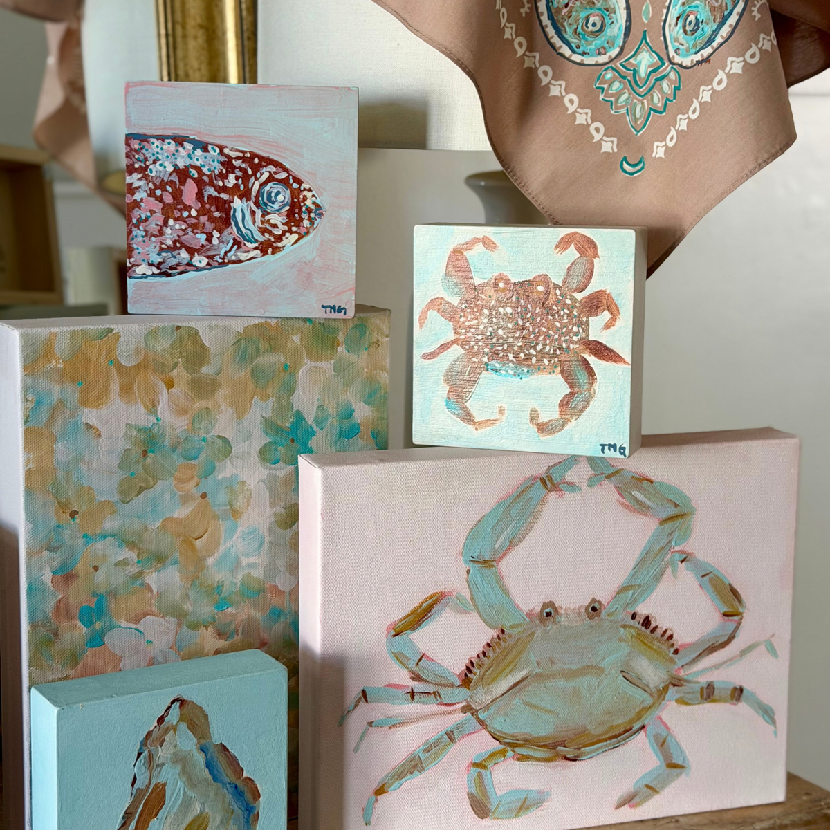 Original coastal artwork by Tracy Marie Grogan featuring a blue crab painting, speckled fish, oyster and abstract canvas in soft turquoise, blush and sandy tones.