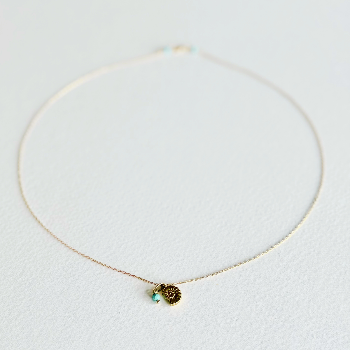 Delicate gold necklace with a small pendant on a light gray background