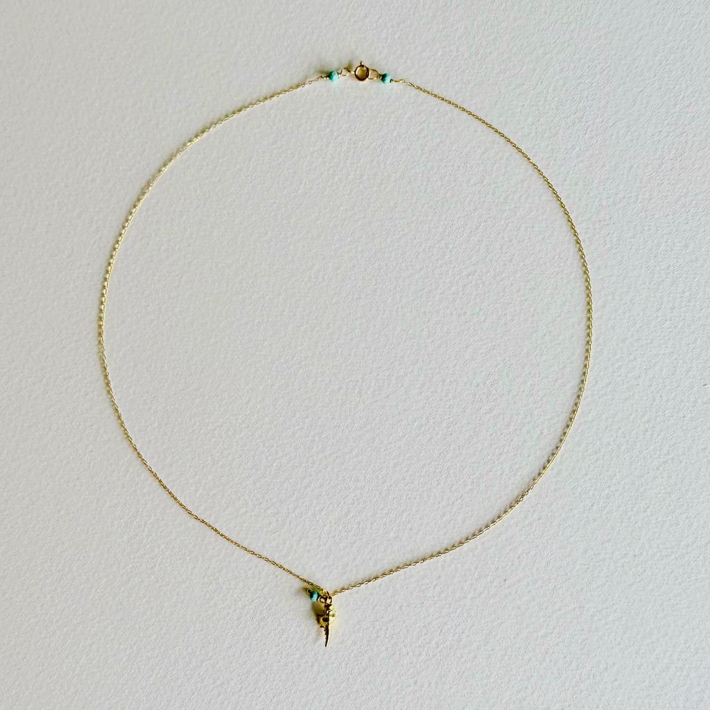 Gold necklace with a small pendant on a light gray background