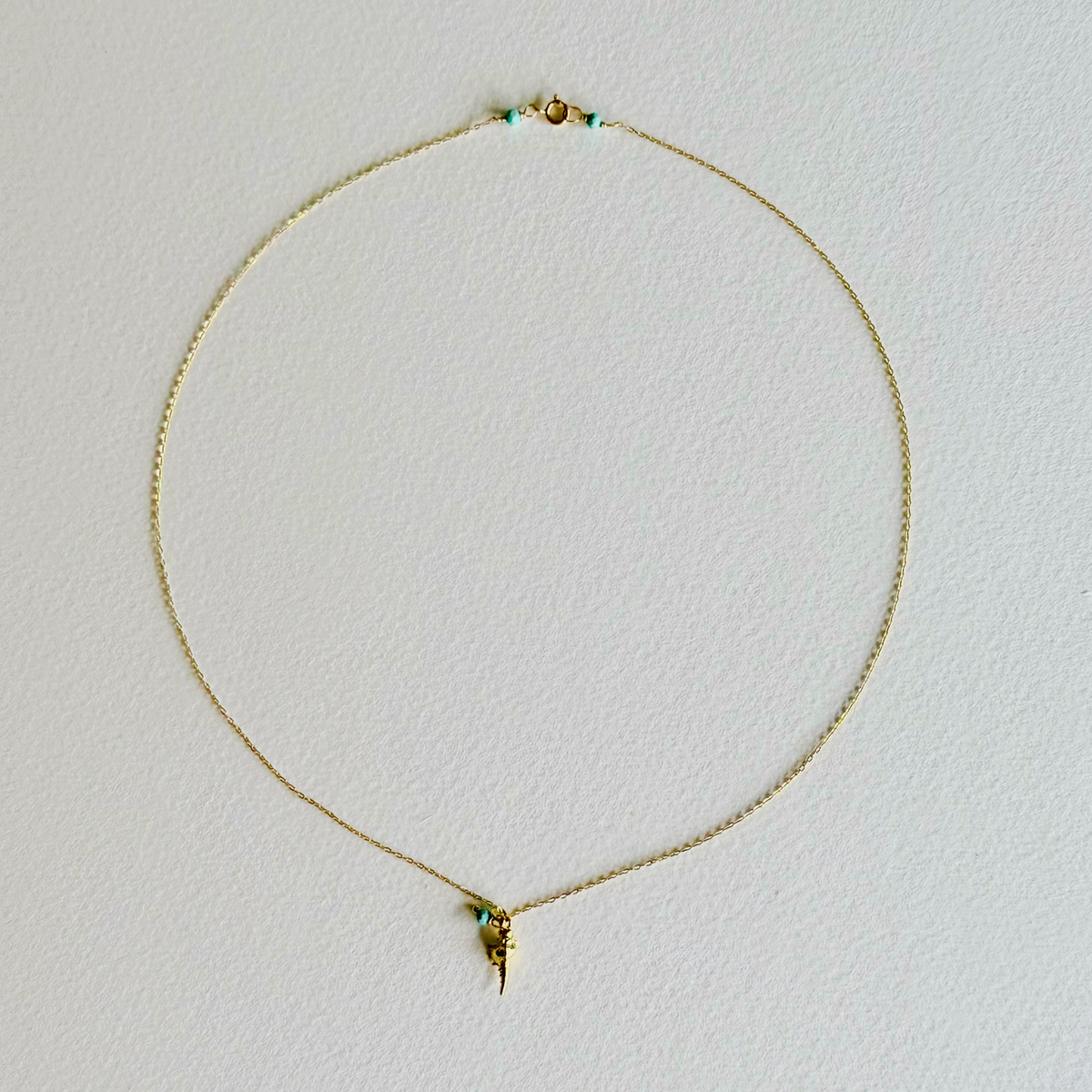 Gold necklace with a small pendant on a light gray background