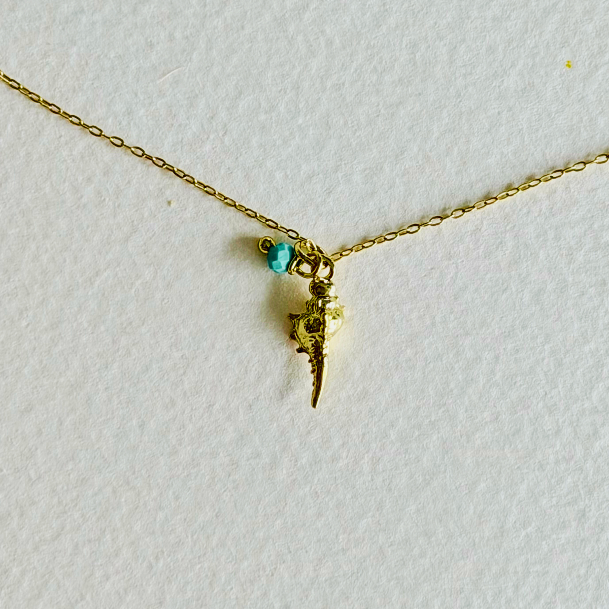 Gold necklace with a small green gemstone and gold charm on a white background