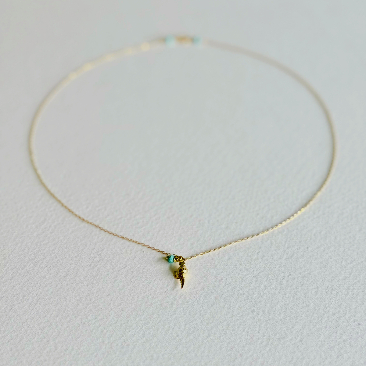 Delicate gold necklace with a small pendant on a light gray background