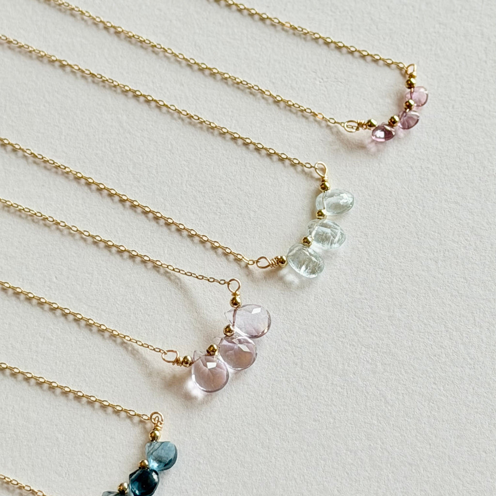 Set of four gold necklaces with various colored gemstones on a light gray background
