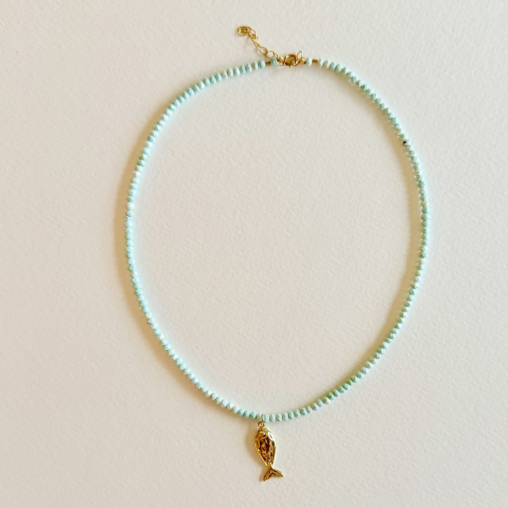 Handmade aqua turquoise beaded necklace with a signature gold fish charm and 14k gold-filled clasp, measuring 16 inches with a 2-inch extender. Inspired by the colors of the sea and handcrafted by Marie & Oakley.