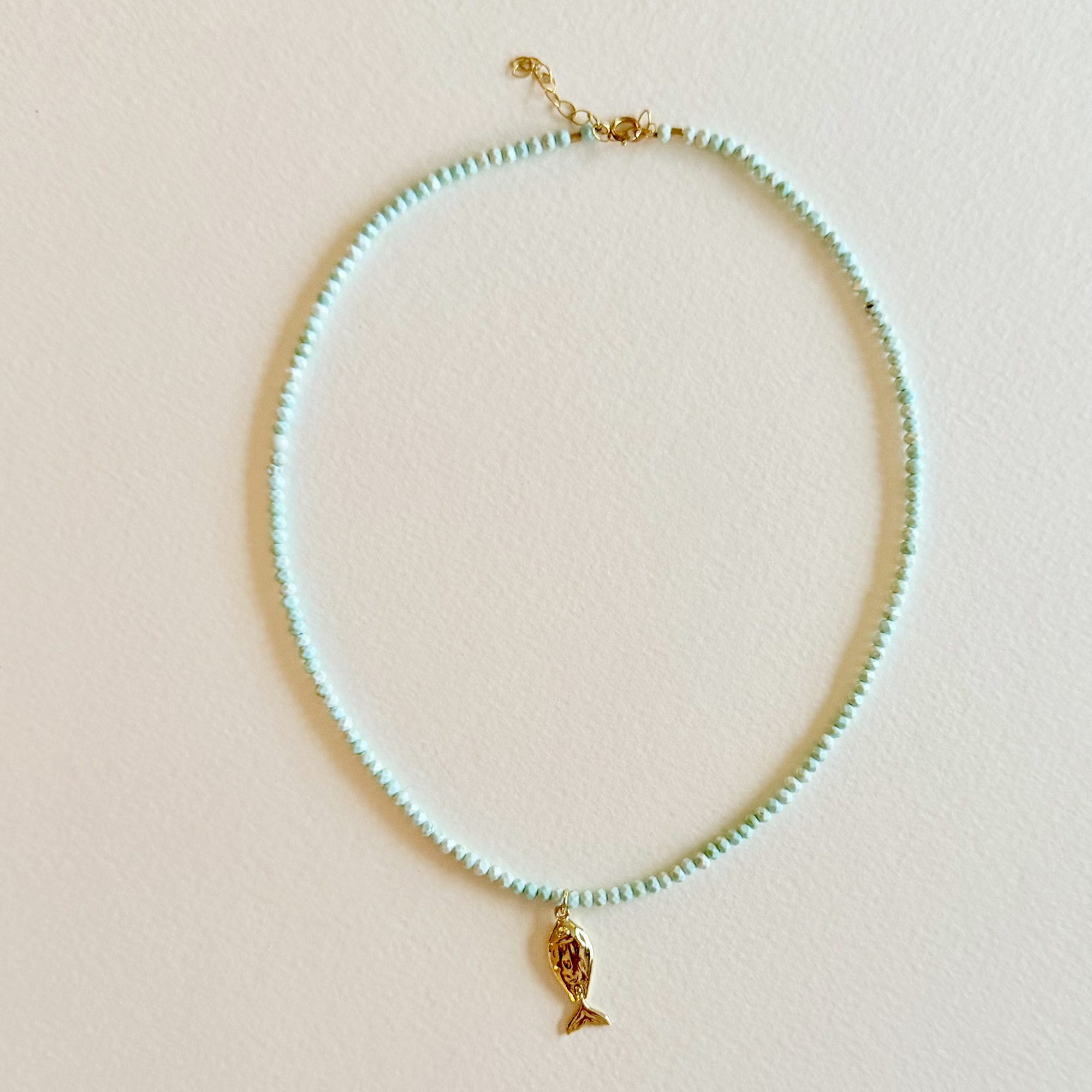 Handmade aqua turquoise beaded necklace with a signature gold fish charm and 14k gold-filled clasp, measuring 16 inches with a 2-inch extender. Inspired by the colors of the sea and handcrafted by Marie & Oakley.