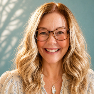 Woman with glasses and blonde hair smiling against a light blue background features the owner and creator of Marie & Oakley 