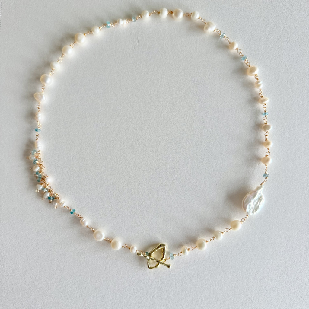Pearl necklace with a gold butterfly clasp on a light gray background