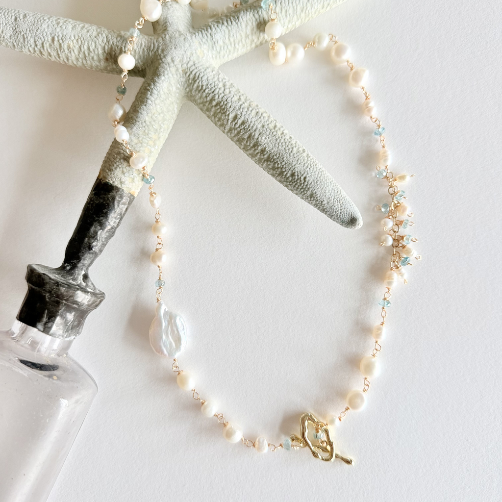 Pearl necklace with a gold clasp on a white surface with starfish and bottle decor.