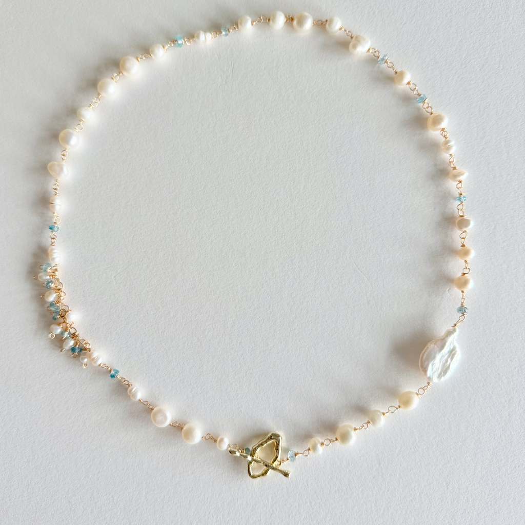 Pearl necklace with a gold butterfly clasp on a light gray background