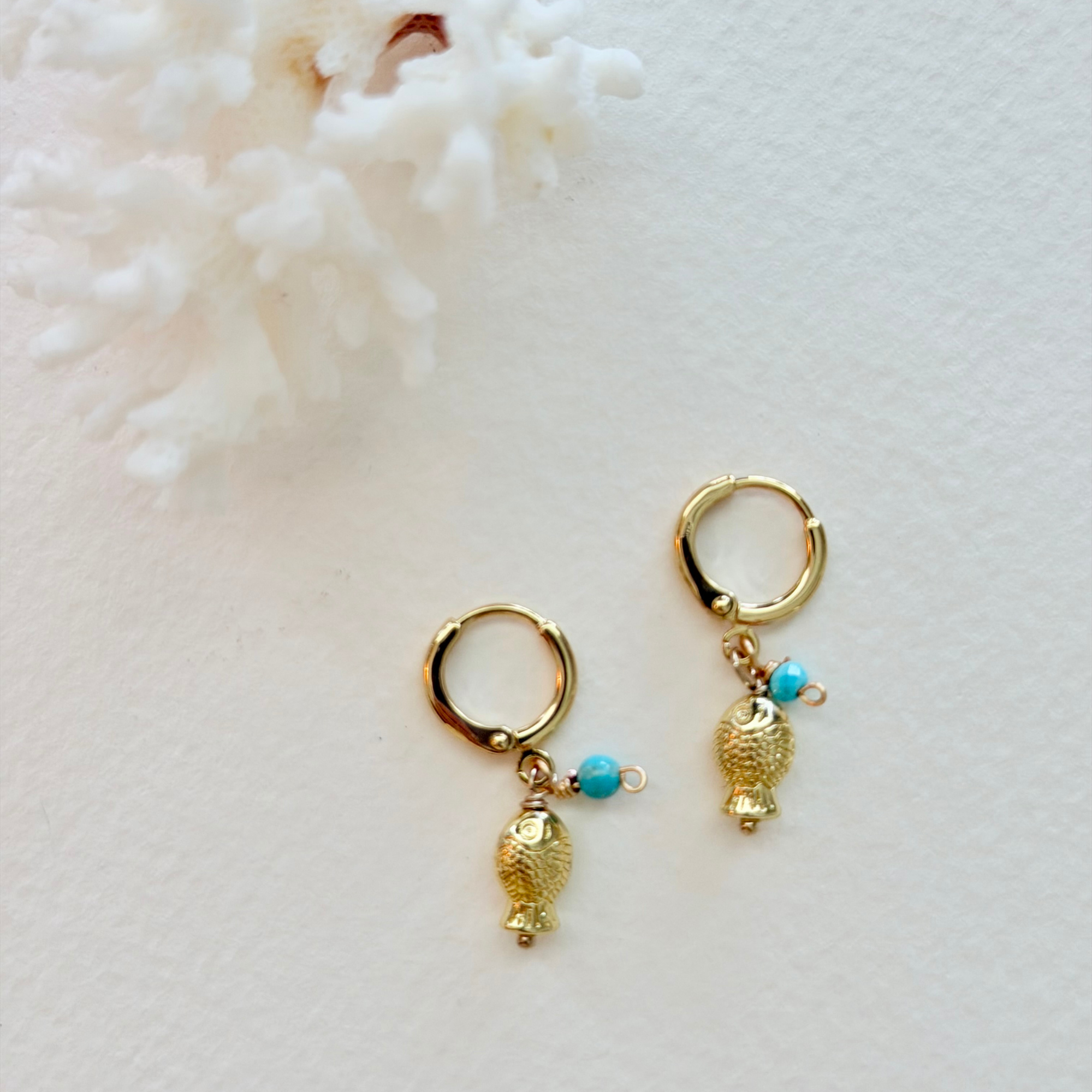 Gold hoop earrings with fish charms on a white background