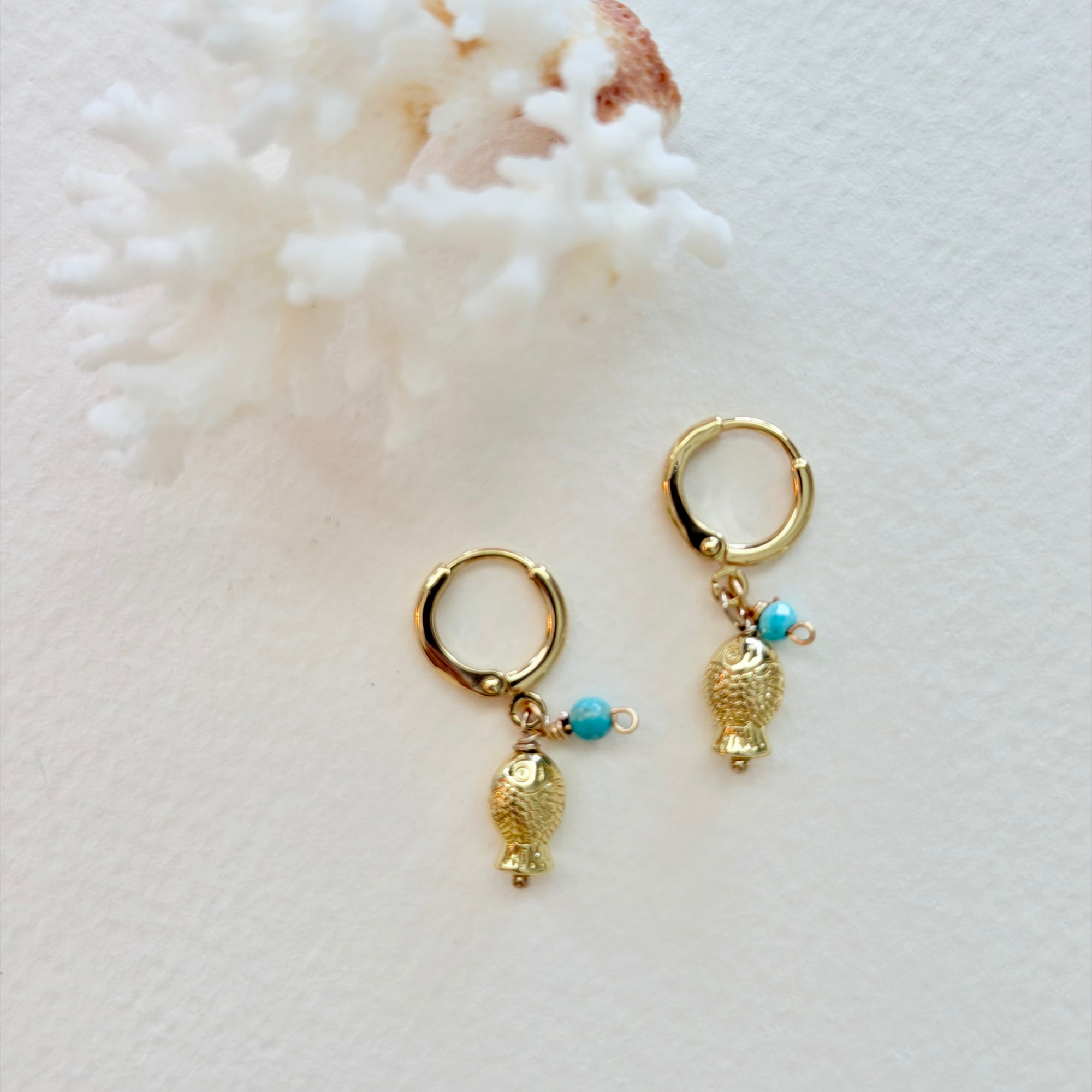 Gold hoop earrings with shell and turquoise bead charms on a white background