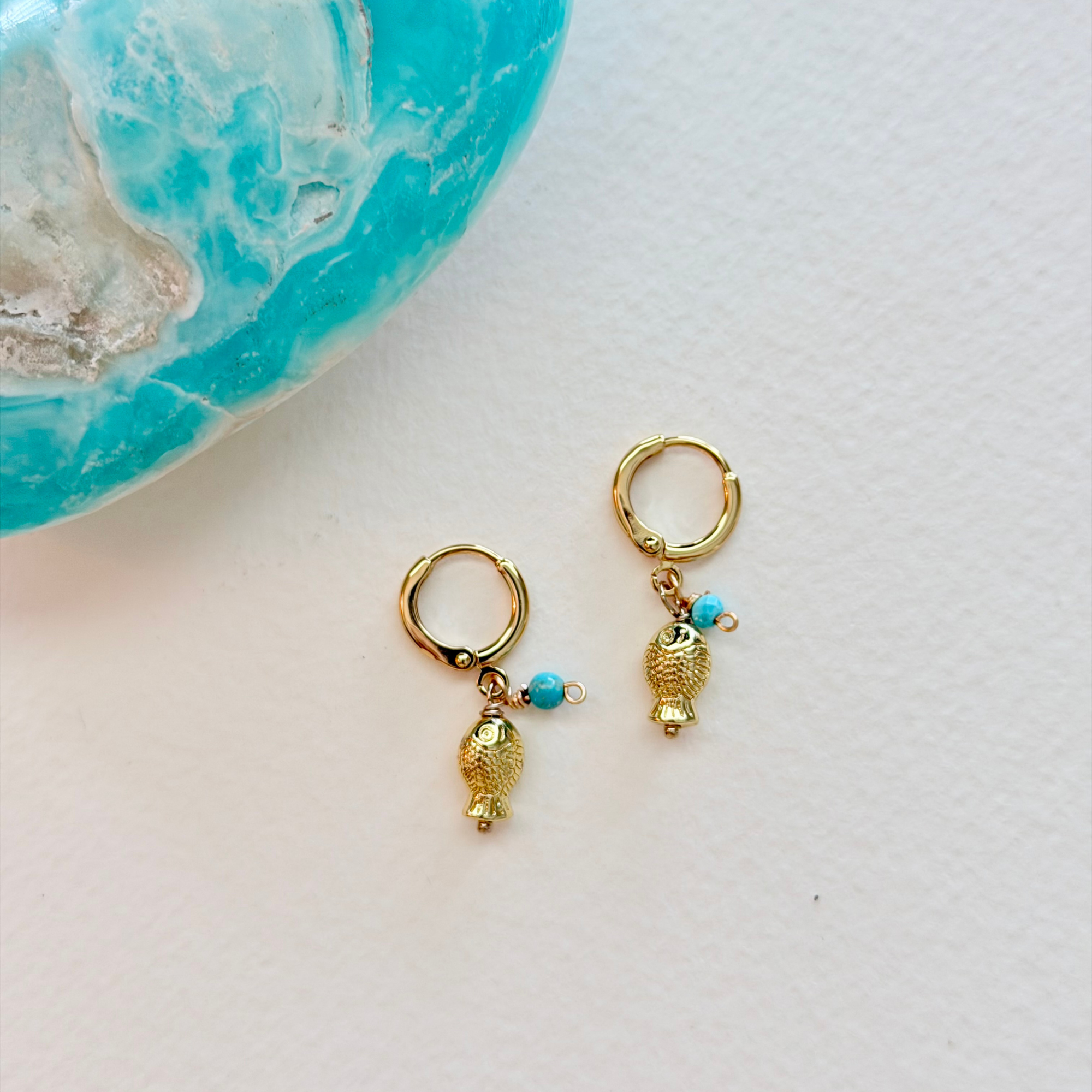 Gold hoop earrings with pineapple-shaped charms on a white surface.