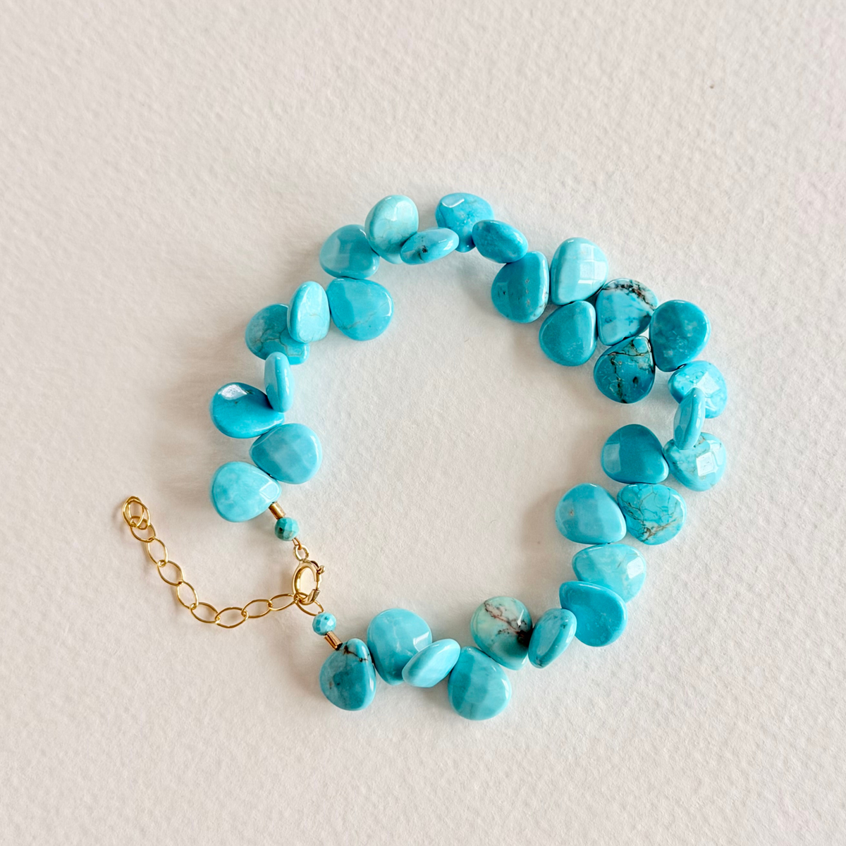 Turquoise beaded bracelet with a gold chain on a light background
