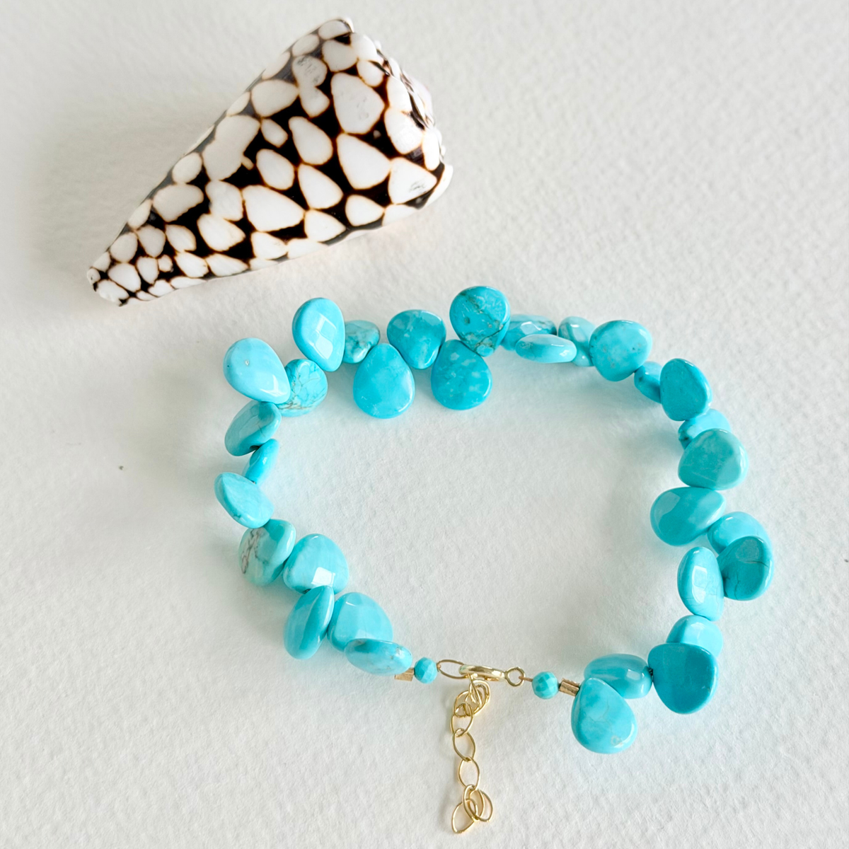 Turquoise beaded bracelet with a gold clasp on a light gray background