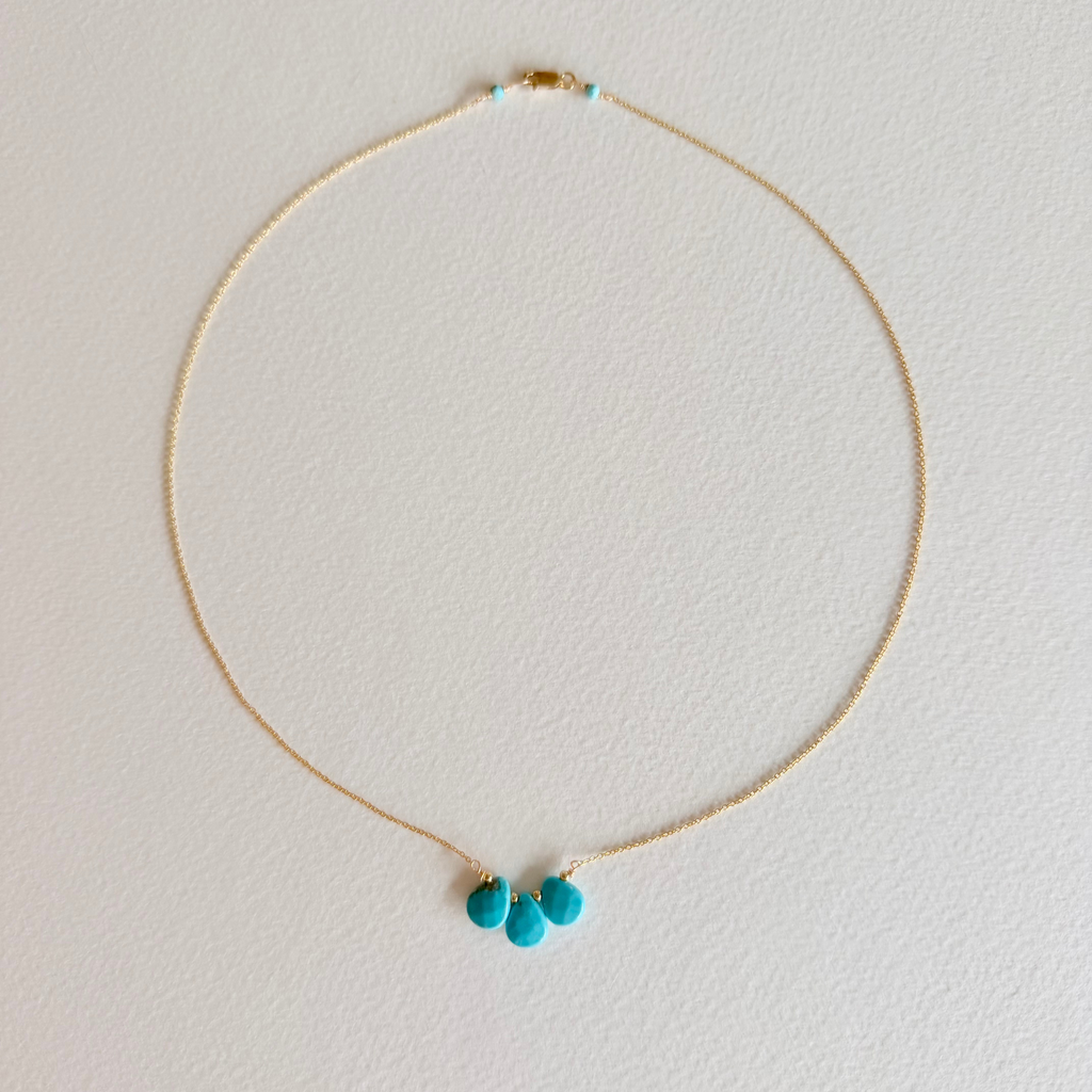 Gold necklace with turquoise pendants on a light gray background