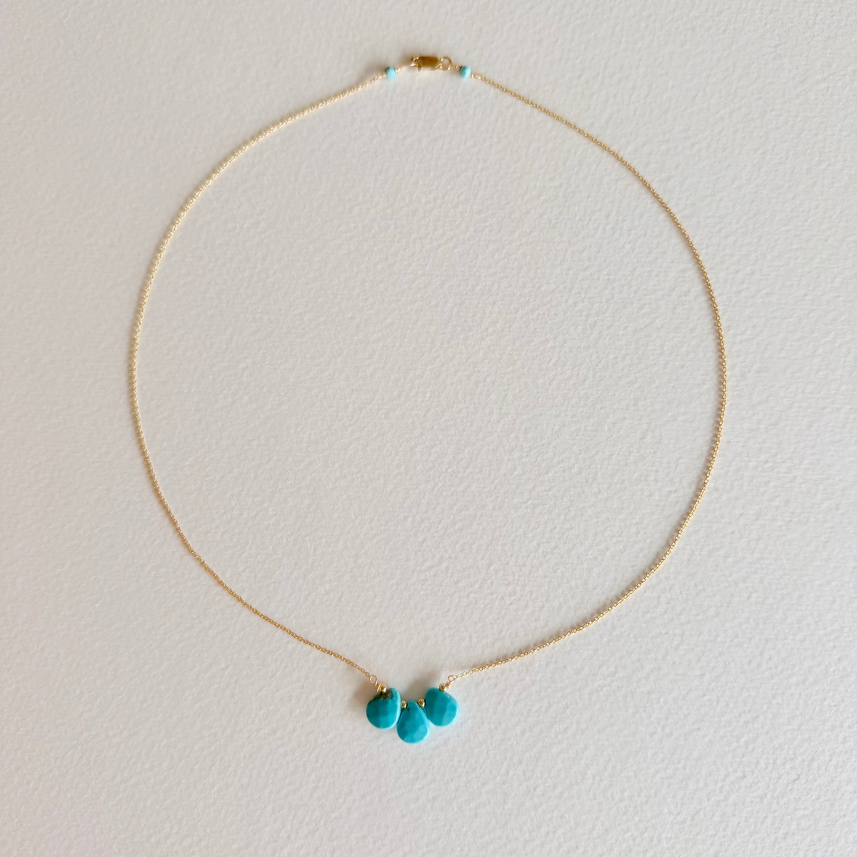Gold necklace with turquoise pendants on a light gray background