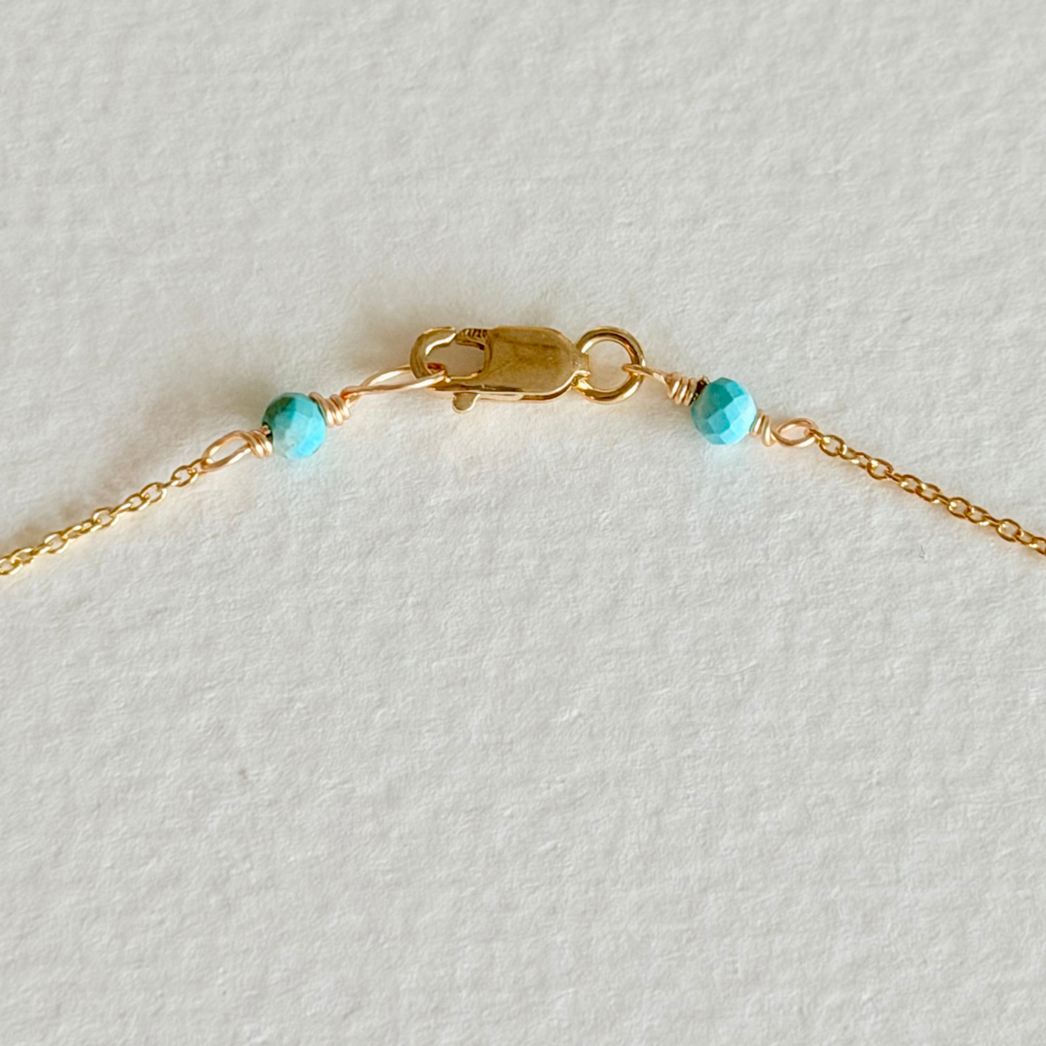 Gold bracelet with turquoise beads on a light gray background