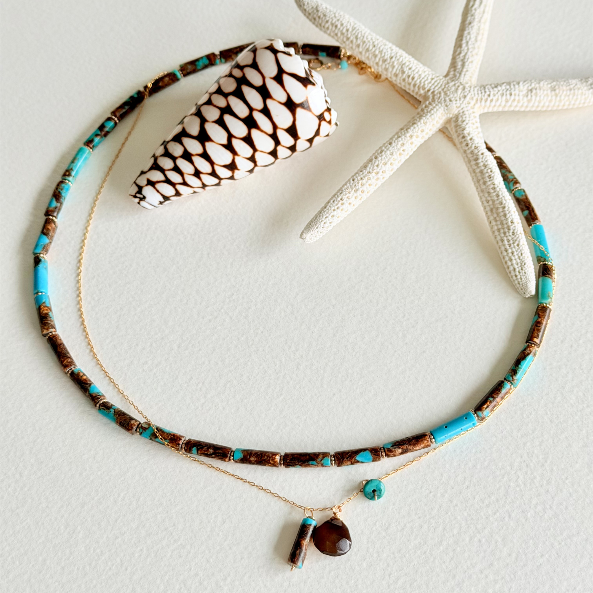 Necklace with turquoise and brown beads on a white surface with a shell and starfish.