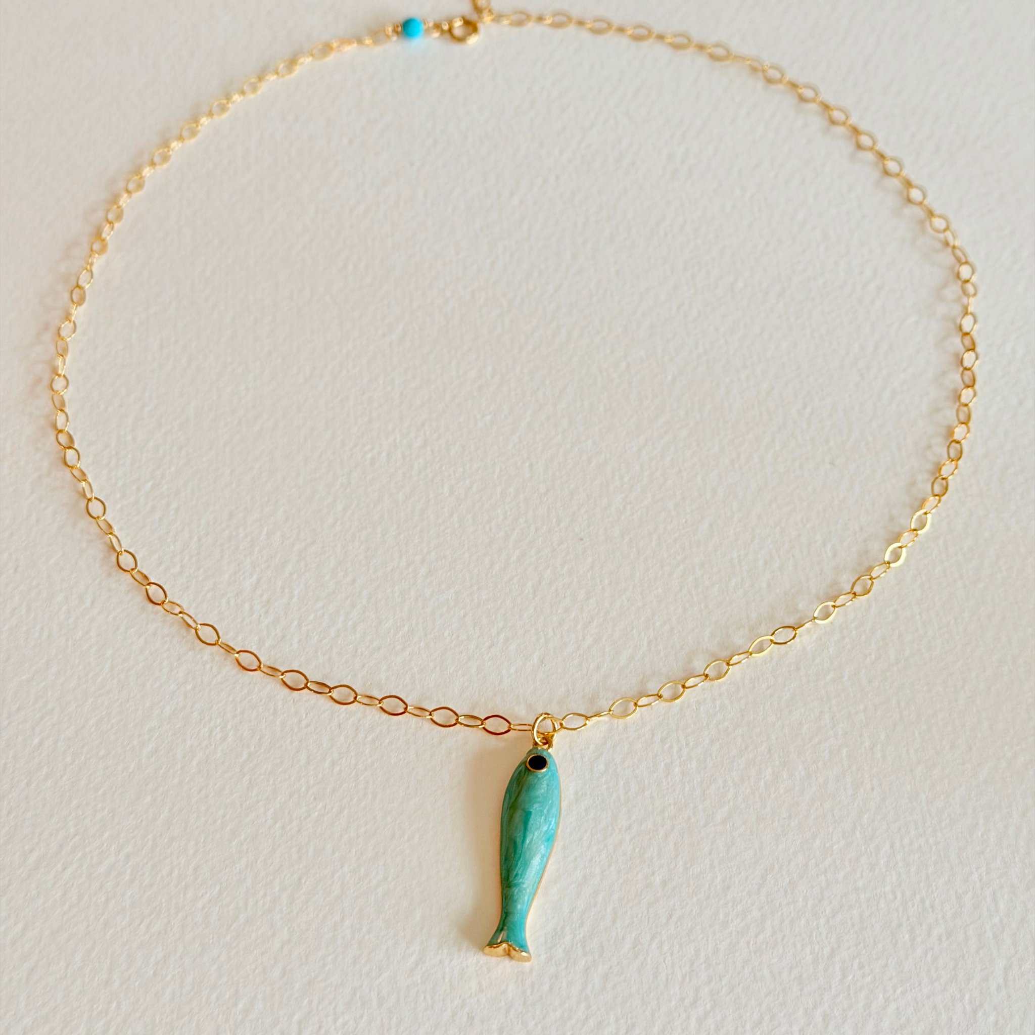 Gold necklace with a turquoise fish pendant on a light gray background