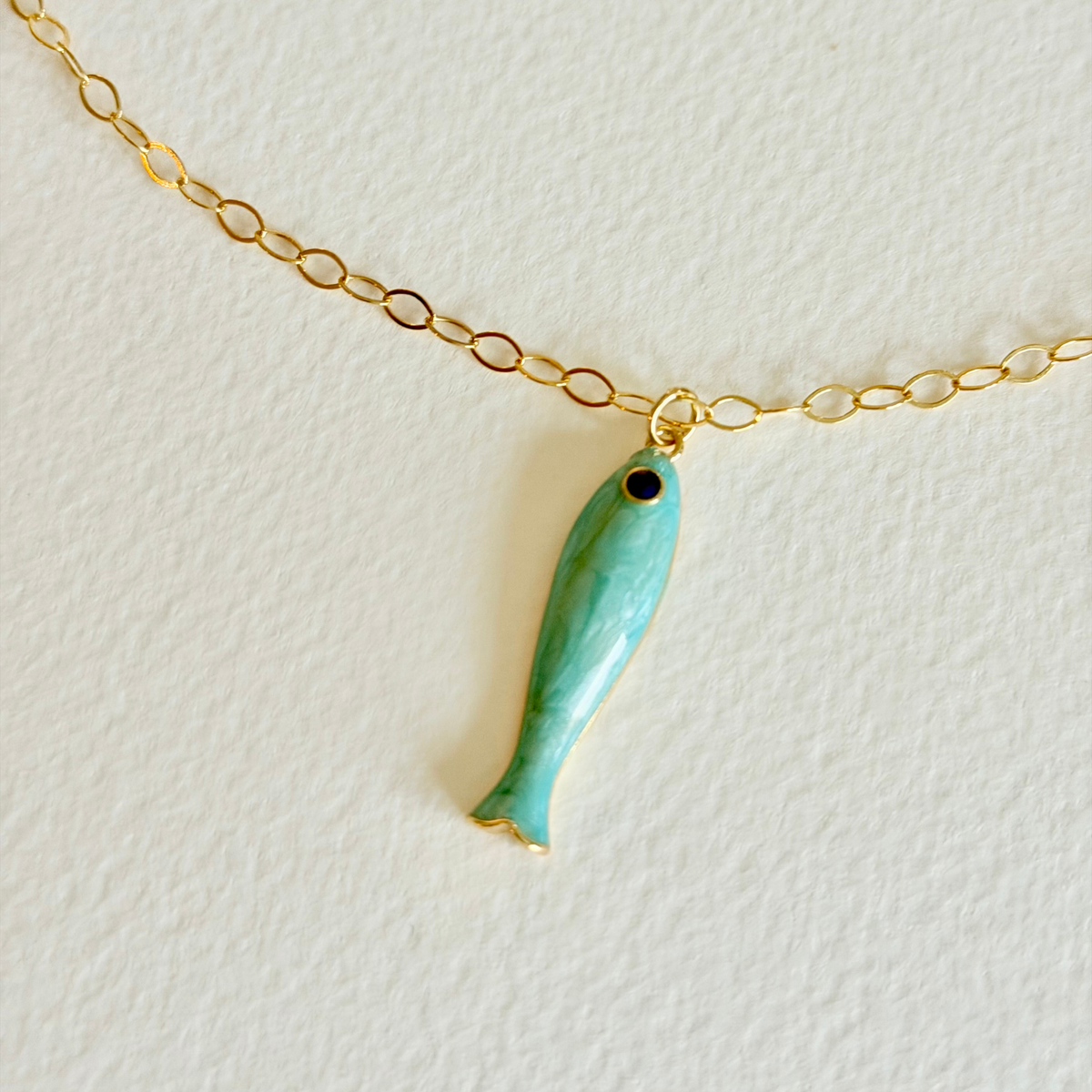 Turquoise fish-shaped pendant on a gold chain against a white background