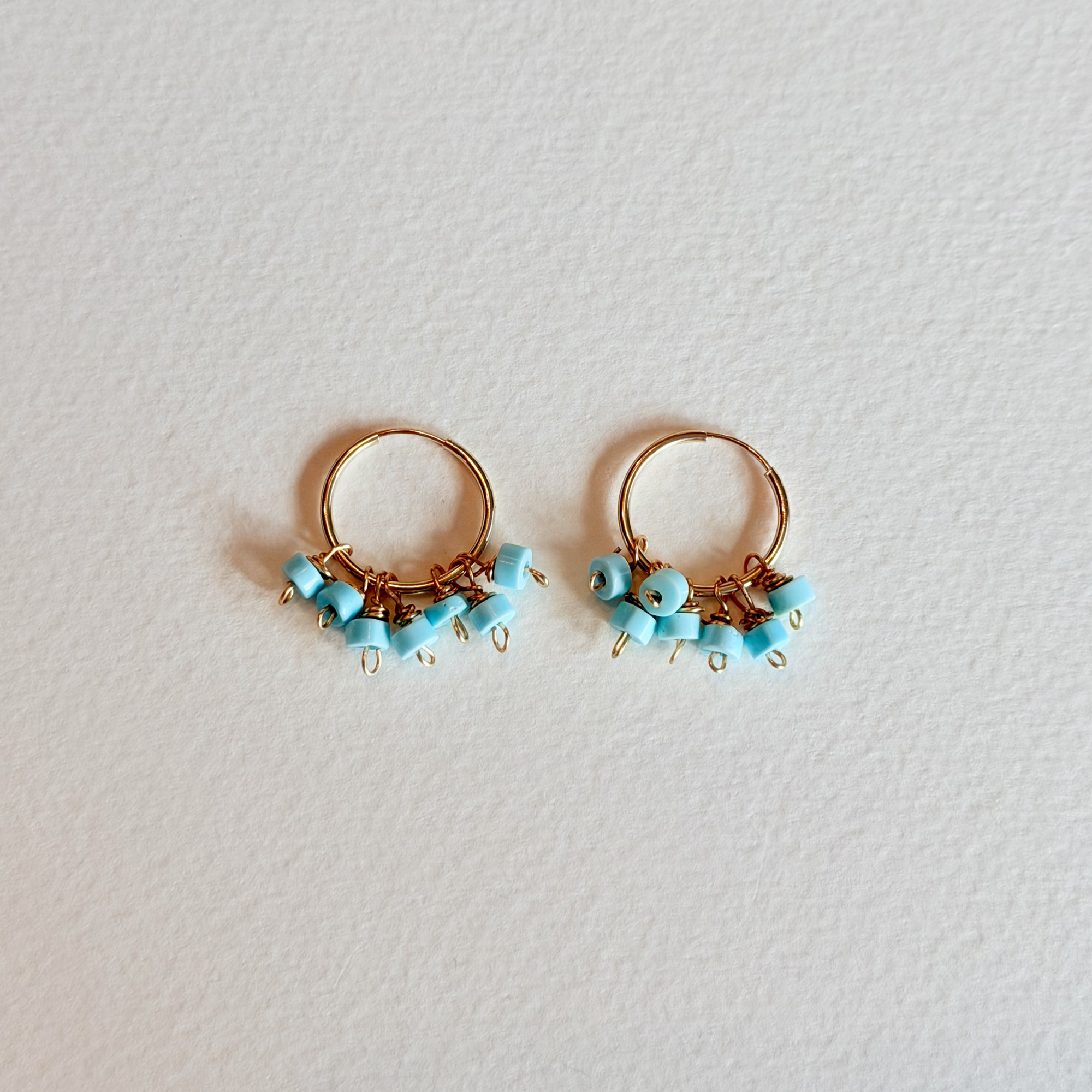 Pair of gold hoop earrings with turquoise beads on a light gray background