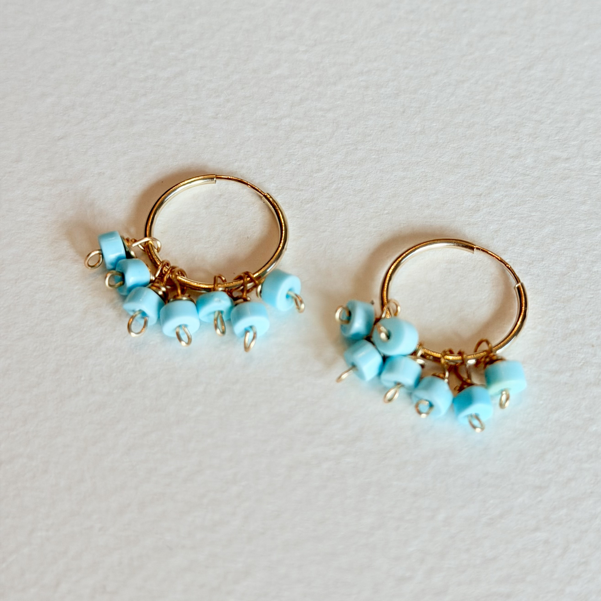 Pair of gold hoop earrings with turquoise beads on a light gray background