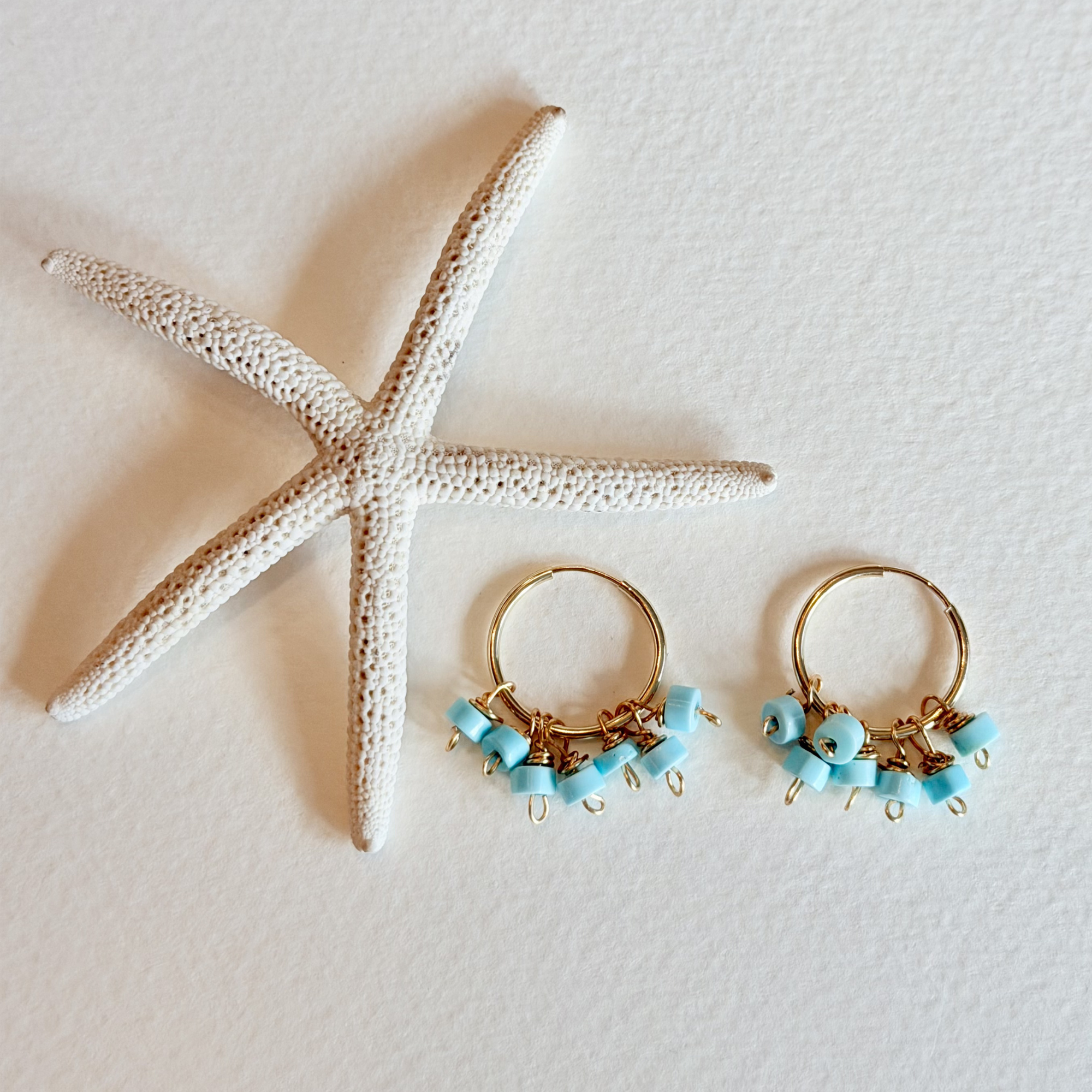 Gold hoop earrings with blue beads next to a starfish on a light background