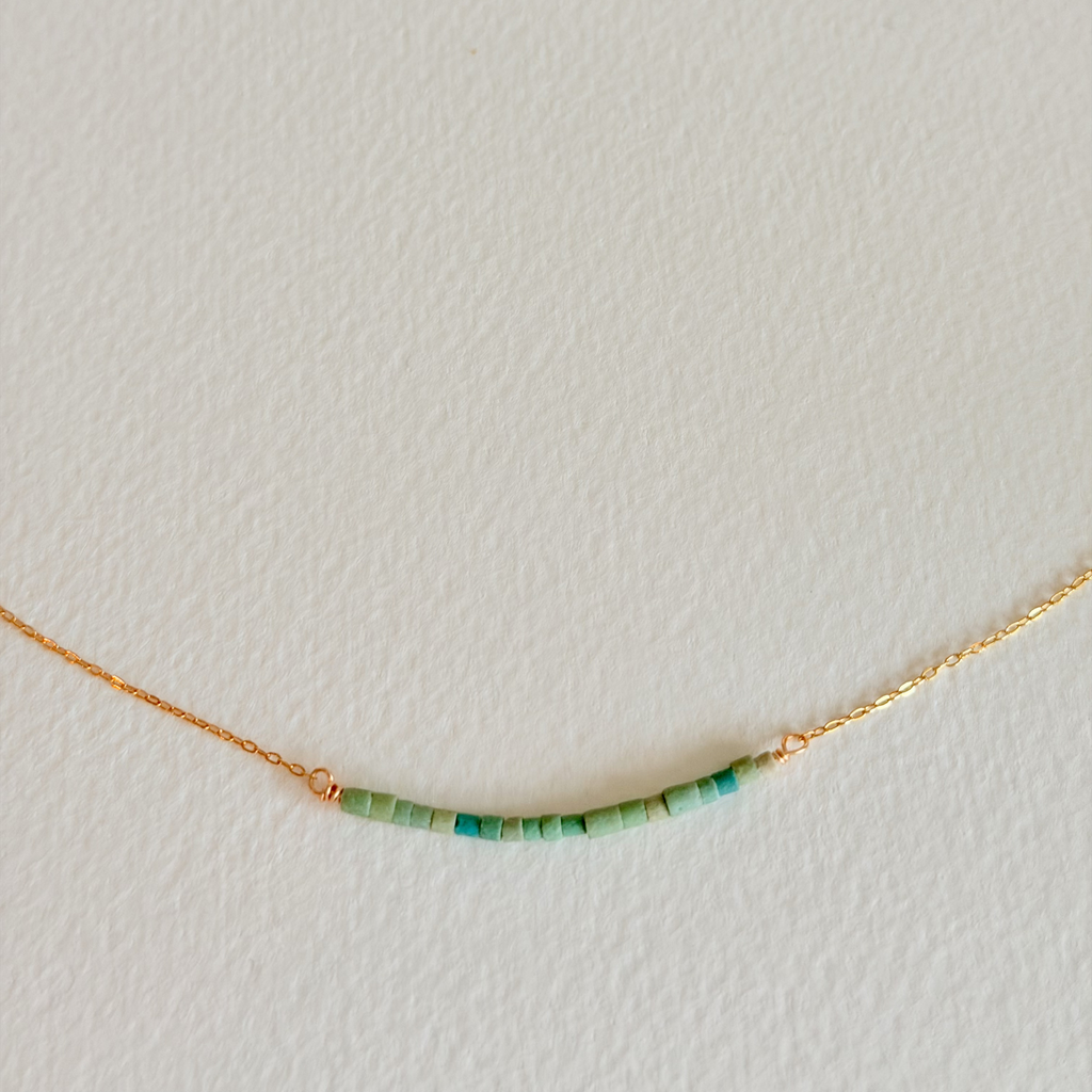 Gold necklace with green beads on a light gray background