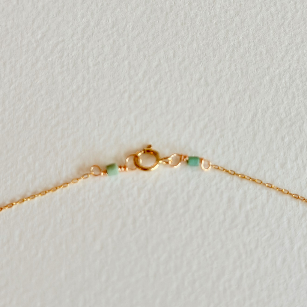 Gold bracelet with green beads on a light gray background