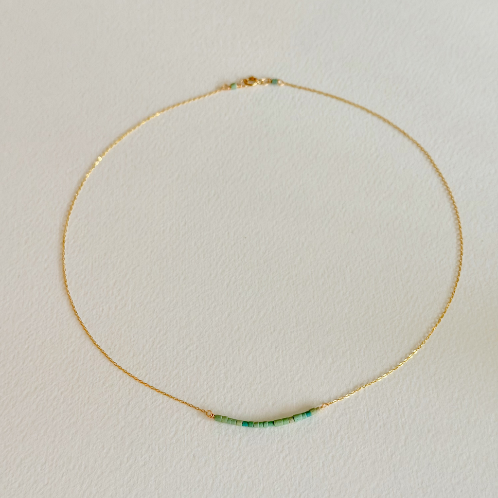 Gold necklace with green beads on a light beige background