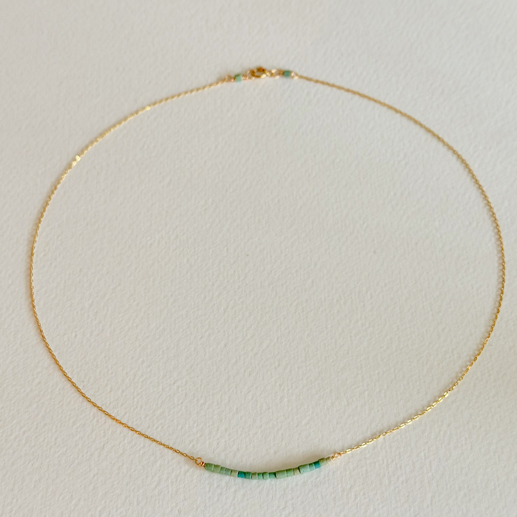 Gold necklace with green and blue beads on a light beige background