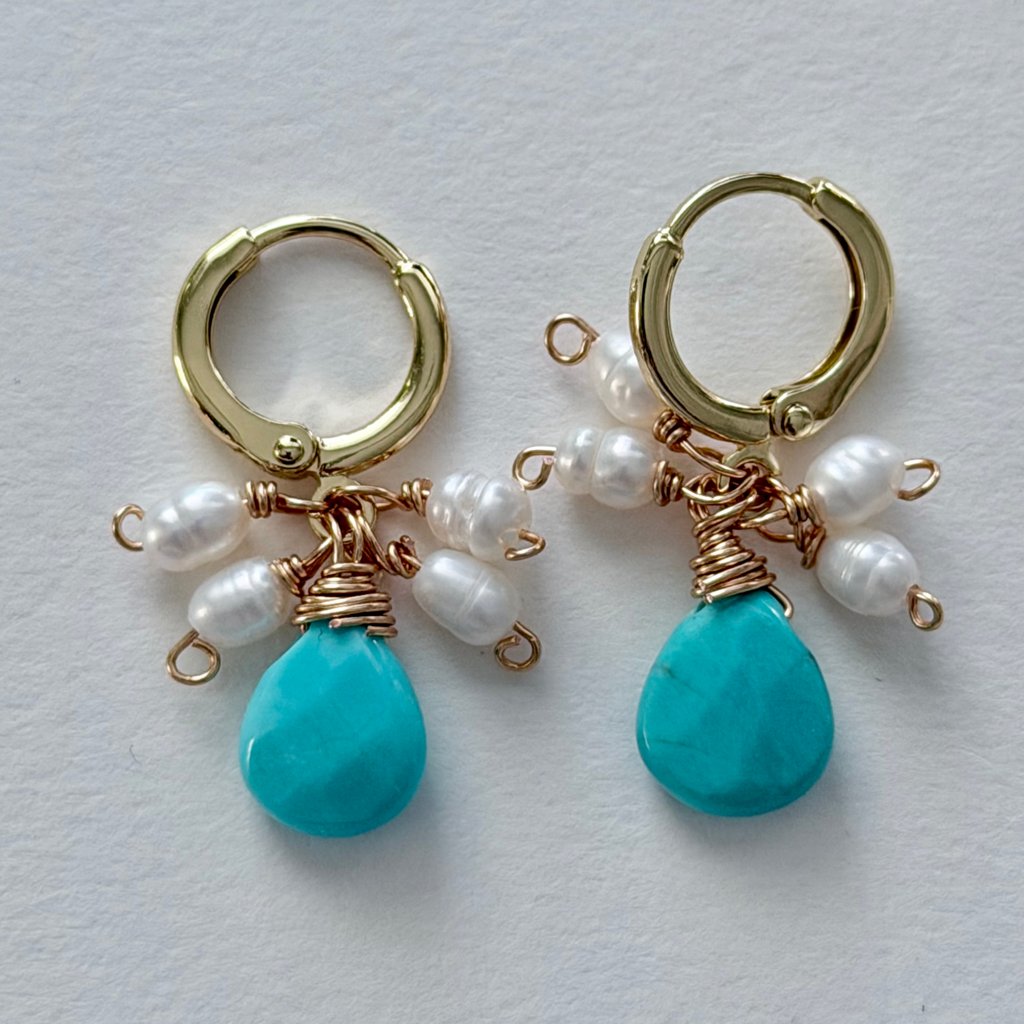 Gold hoop earrings with turquoise drops and pearls on a light gray background