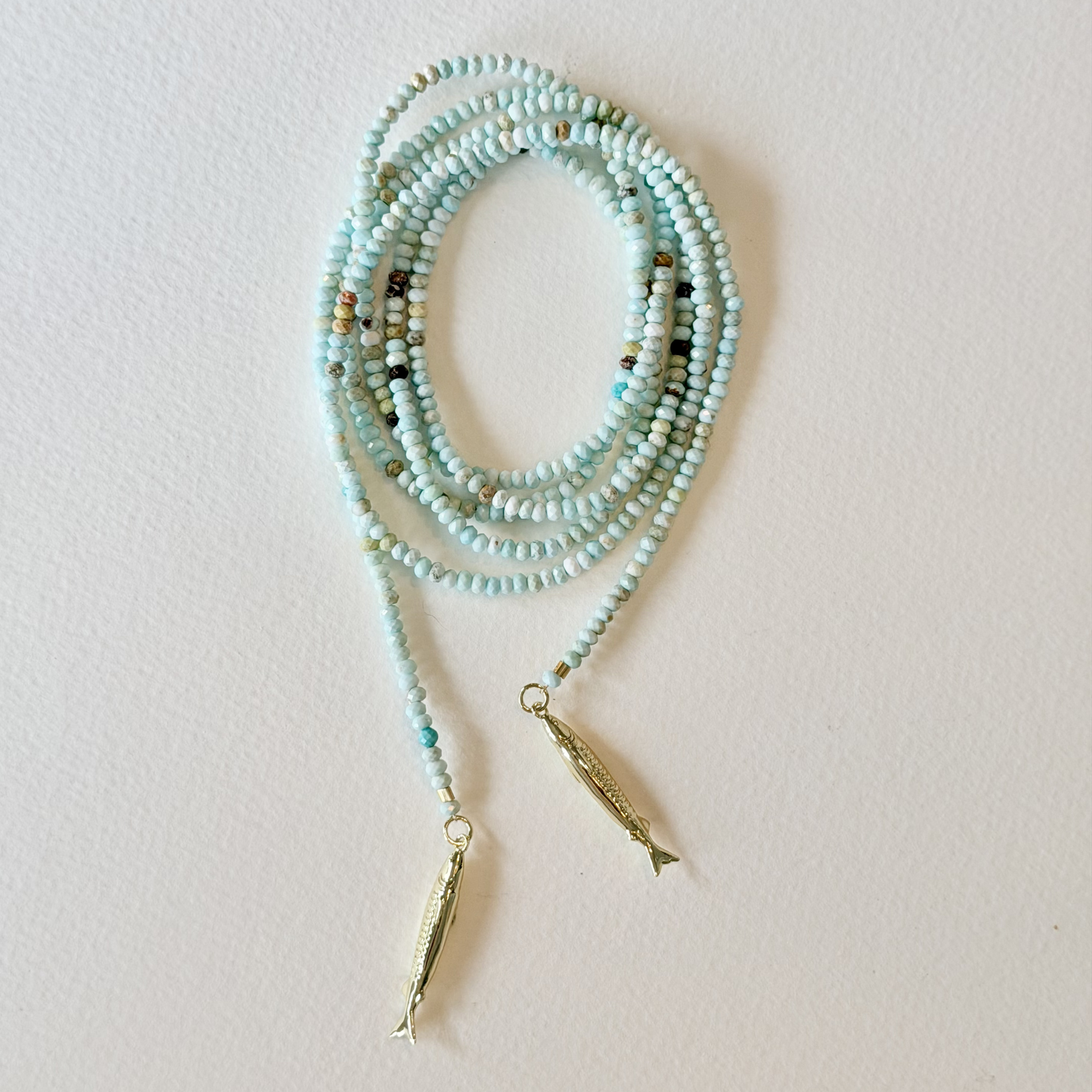 Turquoise beaded necklace with gold pendants on a light background
