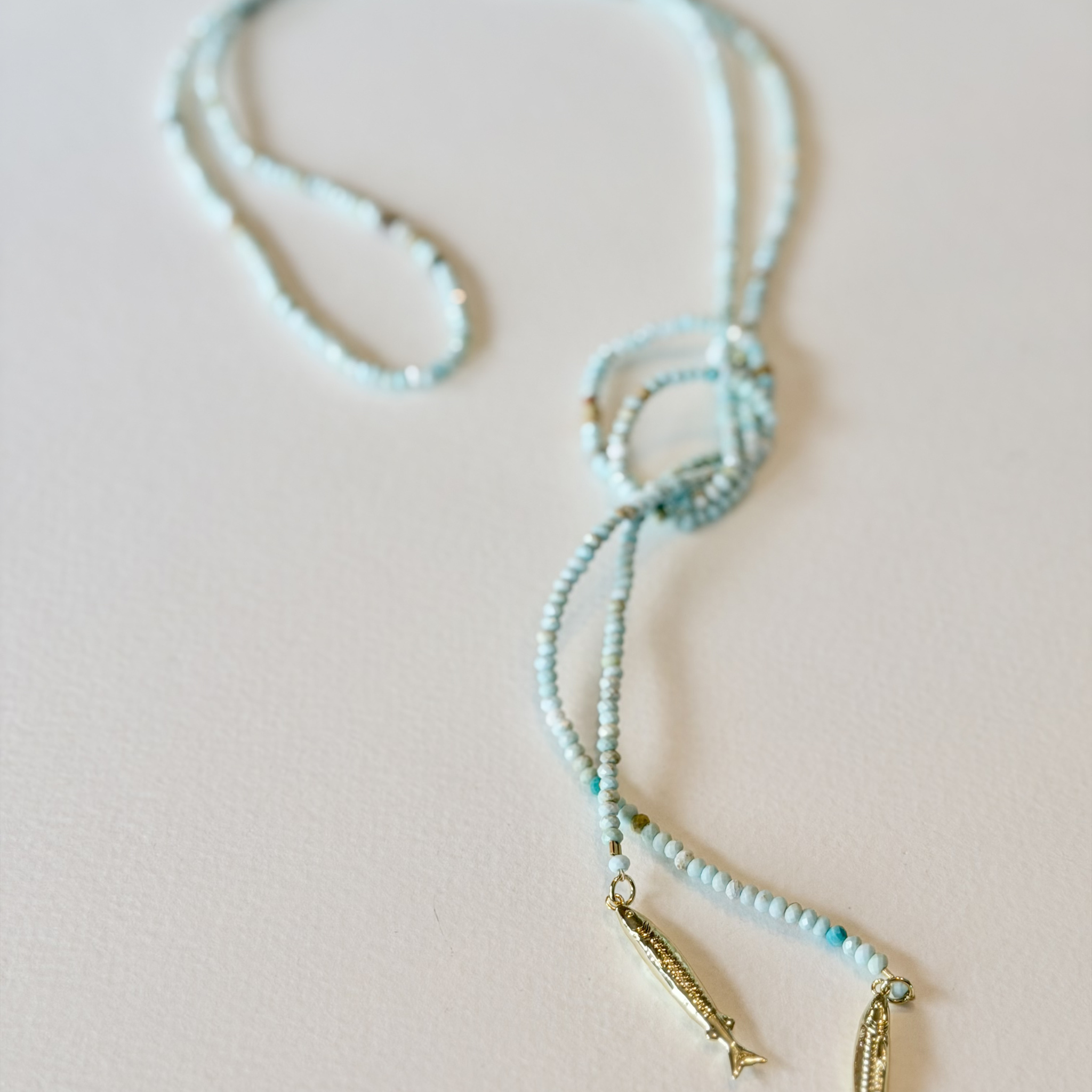 Necklace with blue beads and gold accents on a light pink background