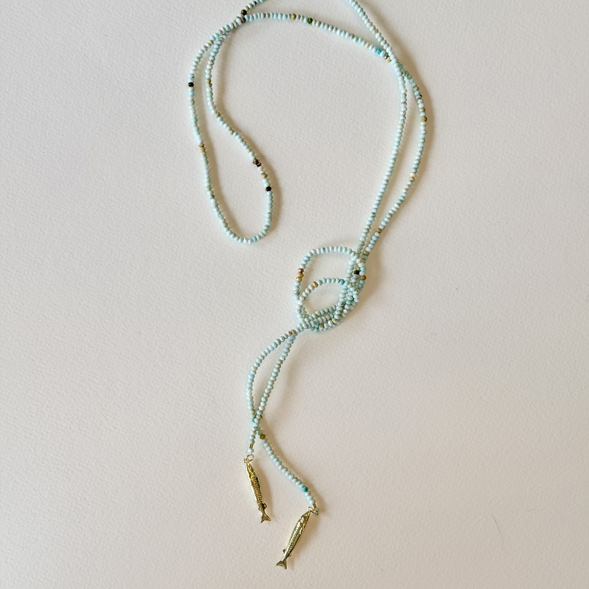 Beaded necklace with fish pendants on a light pink background