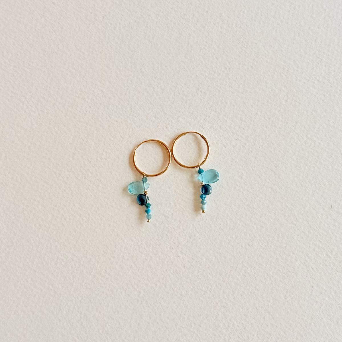 Gold hoop earrings with turquoise and blue bead drops on a light gray background