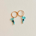 Gold hoop earrings with teal and blue beads on a light beige background