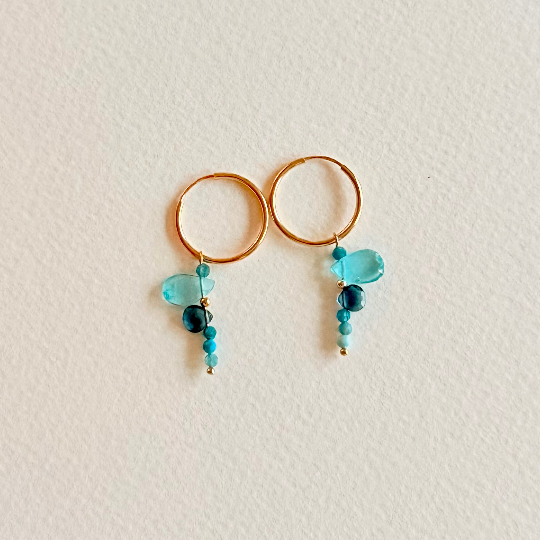 Gold hoop earrings with teal and blue beads on a light beige background