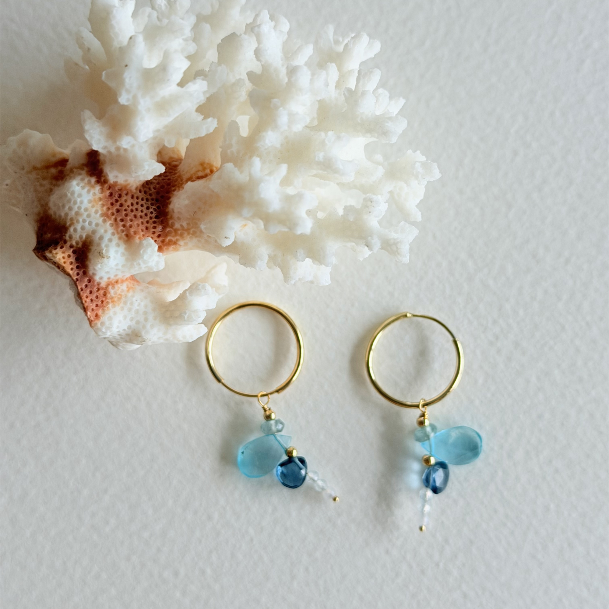 Gold hoop earrings with blue beads on a white background with coral.