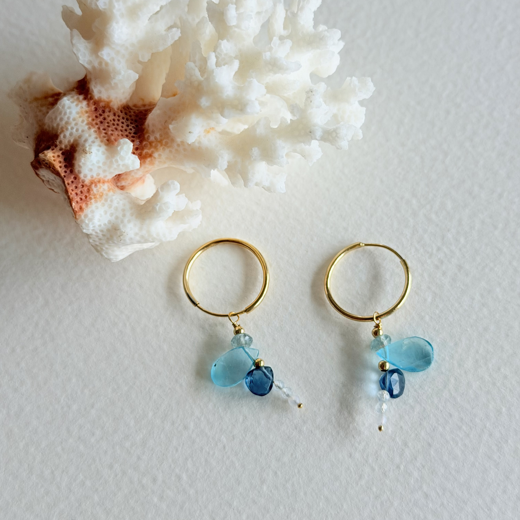 Gold hoop earrings with blue beads on a textured white surface