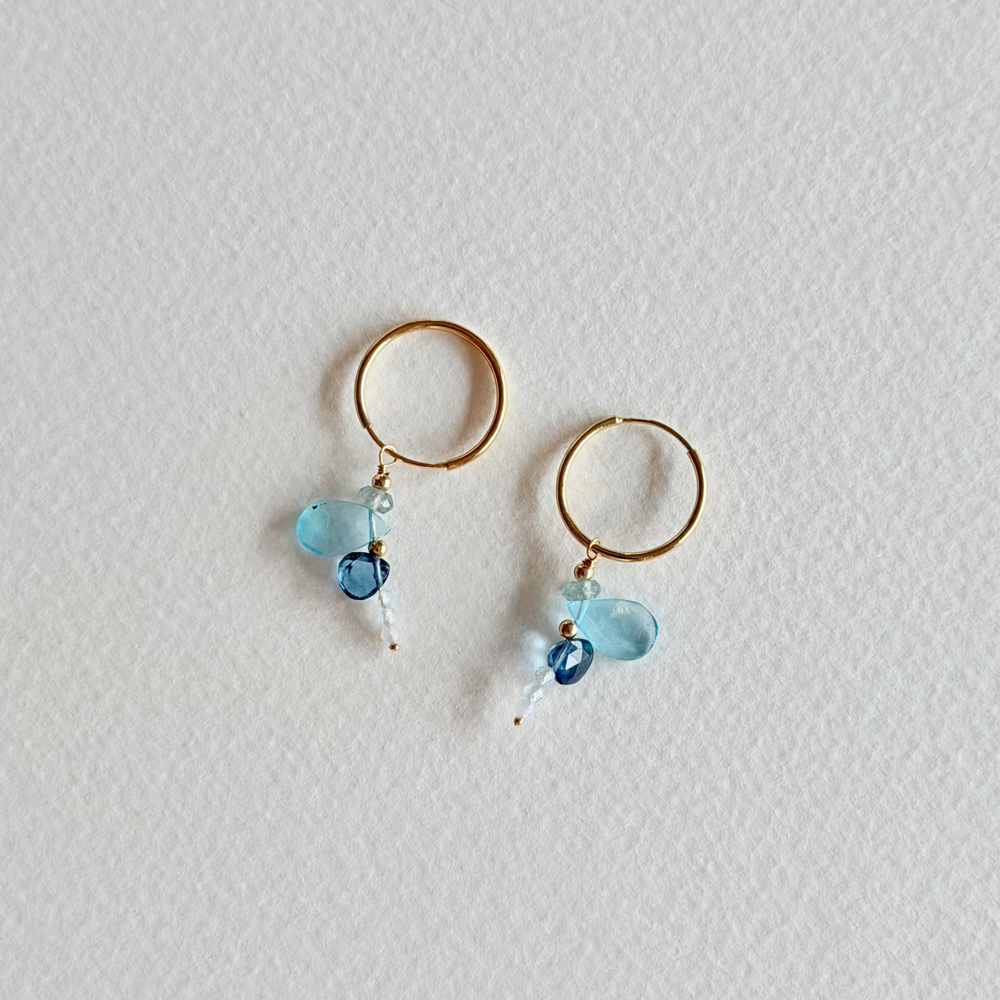 Gold hoop earrings with blue beads on a light gray background