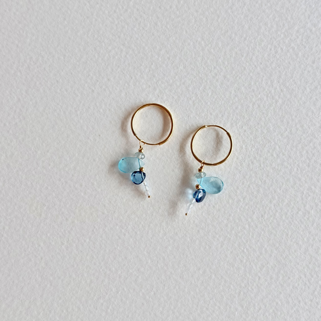 Gold hoop earrings with blue beads on a light gray background