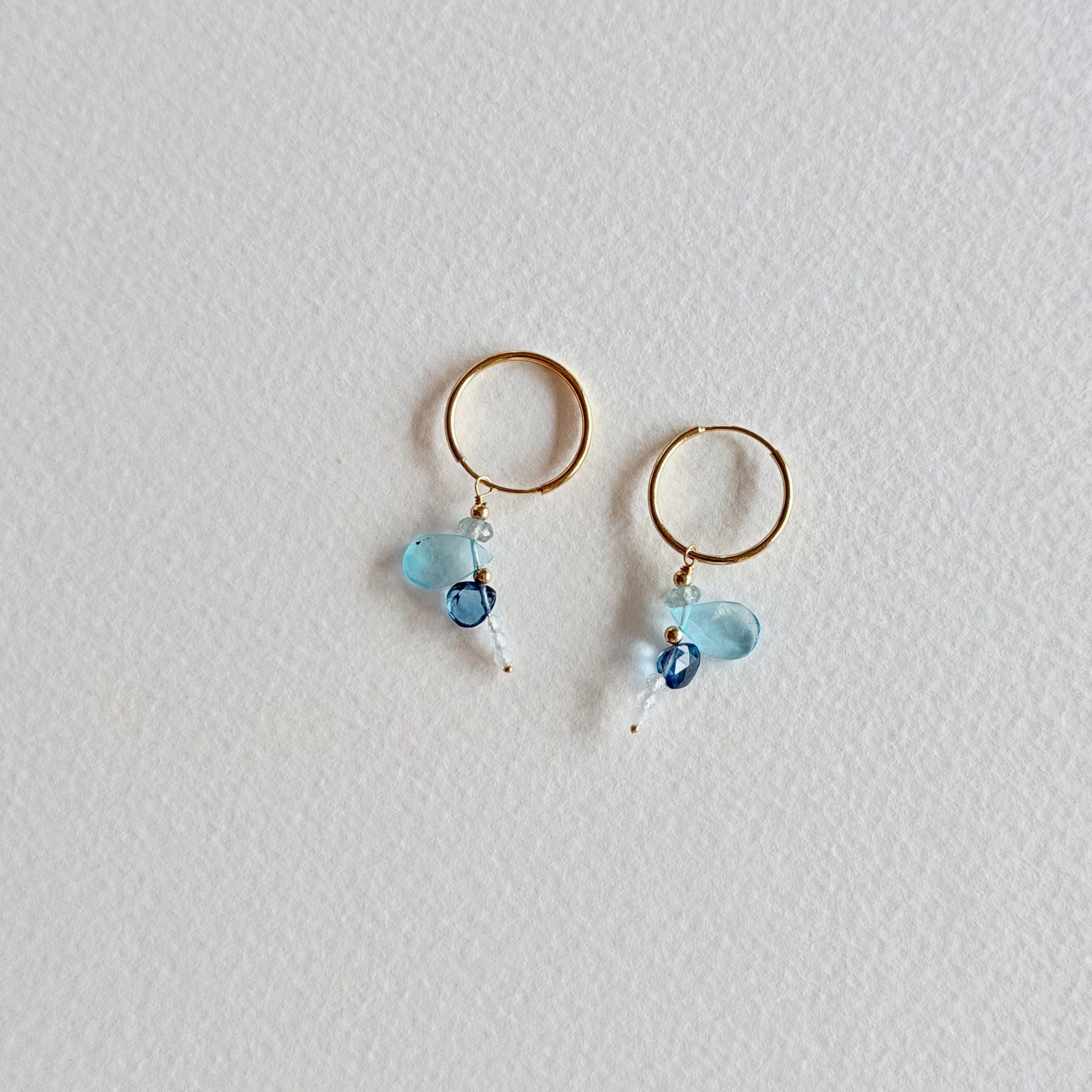 Gold hoop earrings with blue beads on a light gray background