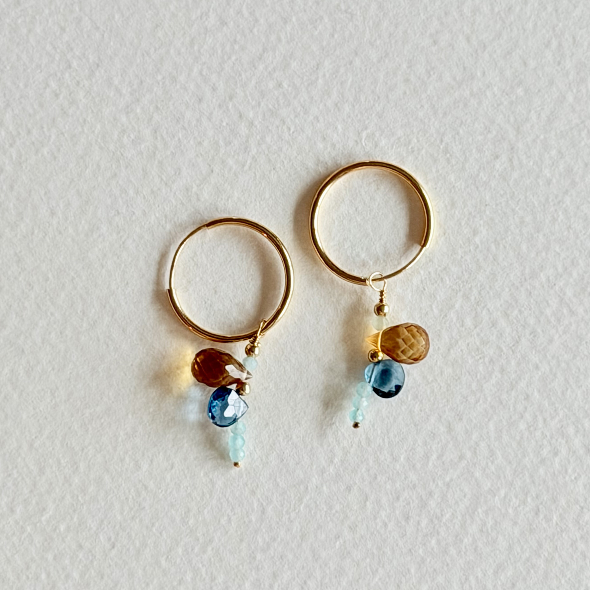 Gold hoop earrings with blue and brown beads on a light gray background